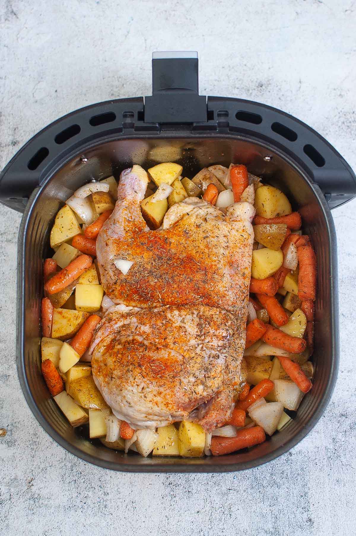 Raw chicken on top of the vegetables in the air fryer basket.