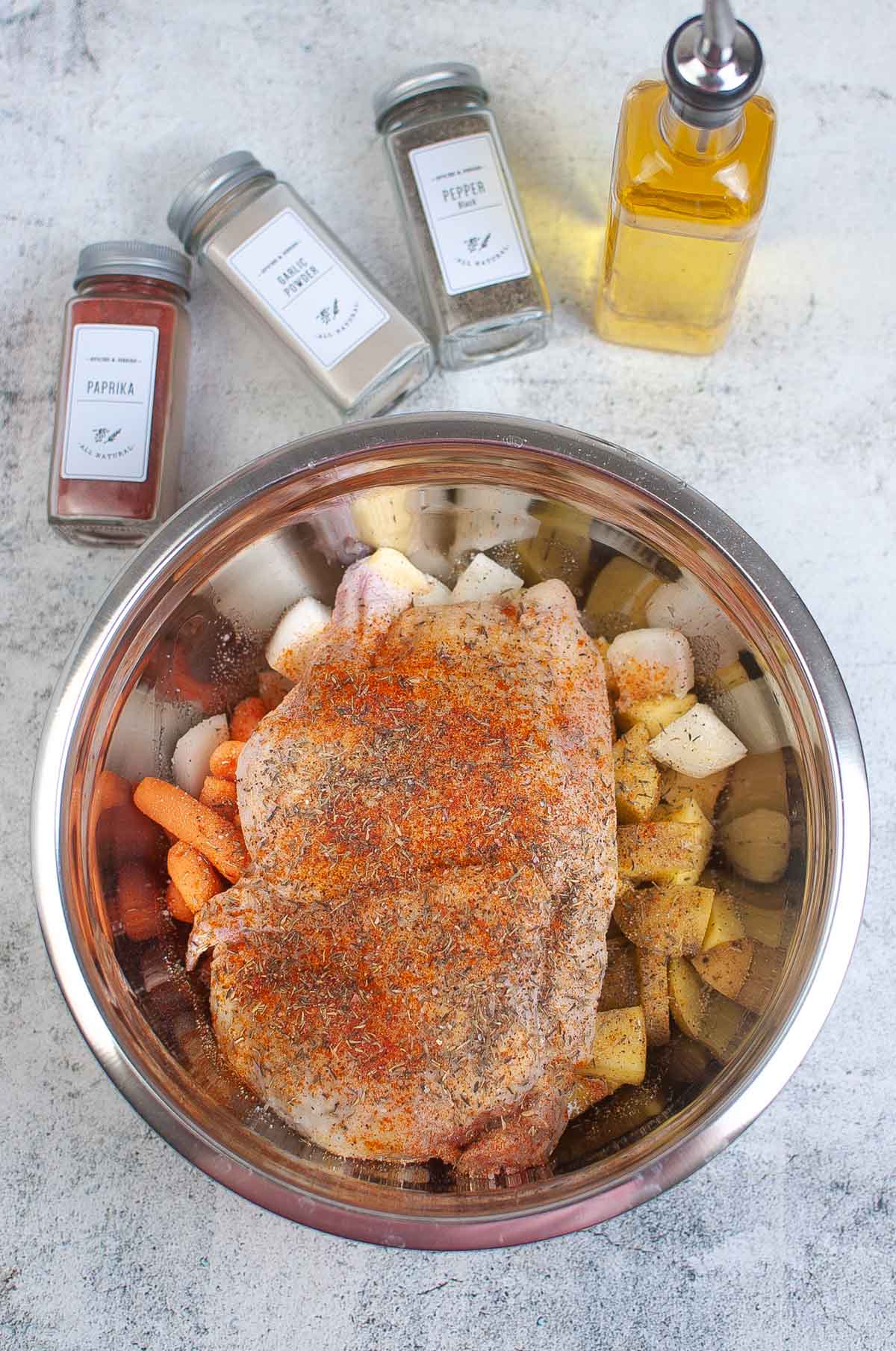 Raw half chicken in a bowl with vegetables and topped with spices.