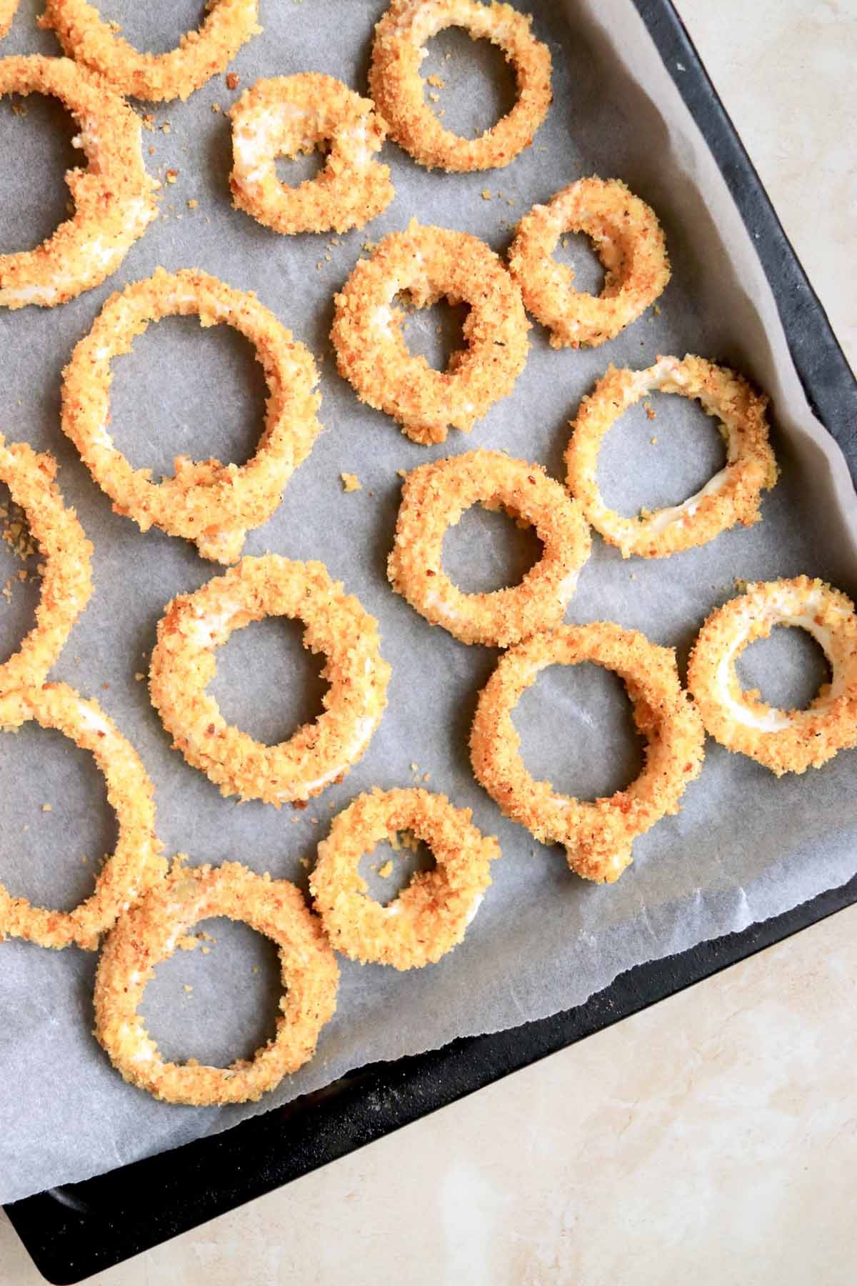Unbaked onion rings on a parchment lined baking sheet.