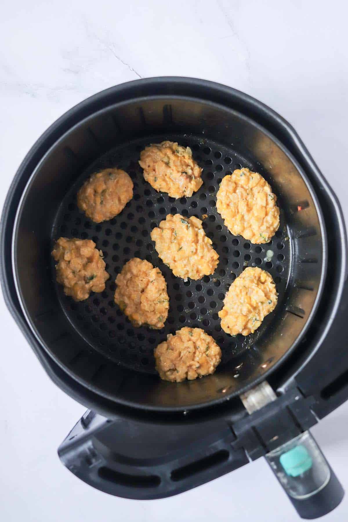 Uncooked corn fritters in the air fryer basket.