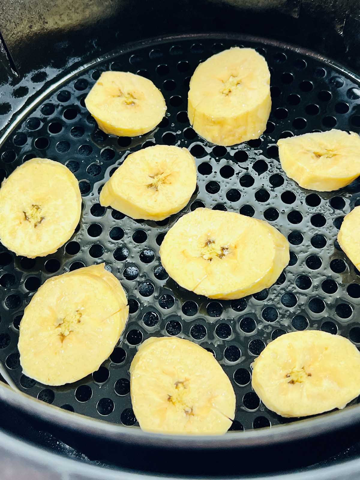 Uncooked plantain slices in the air fryer basket.