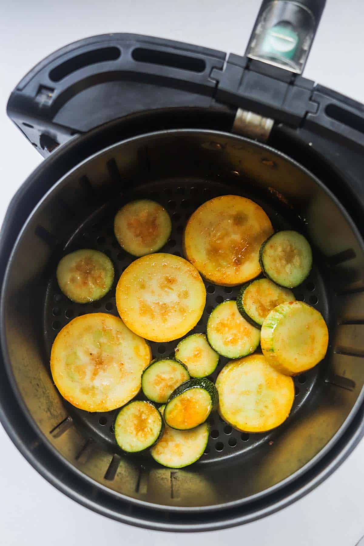Uncooked slices of squash in the air fryer basket.