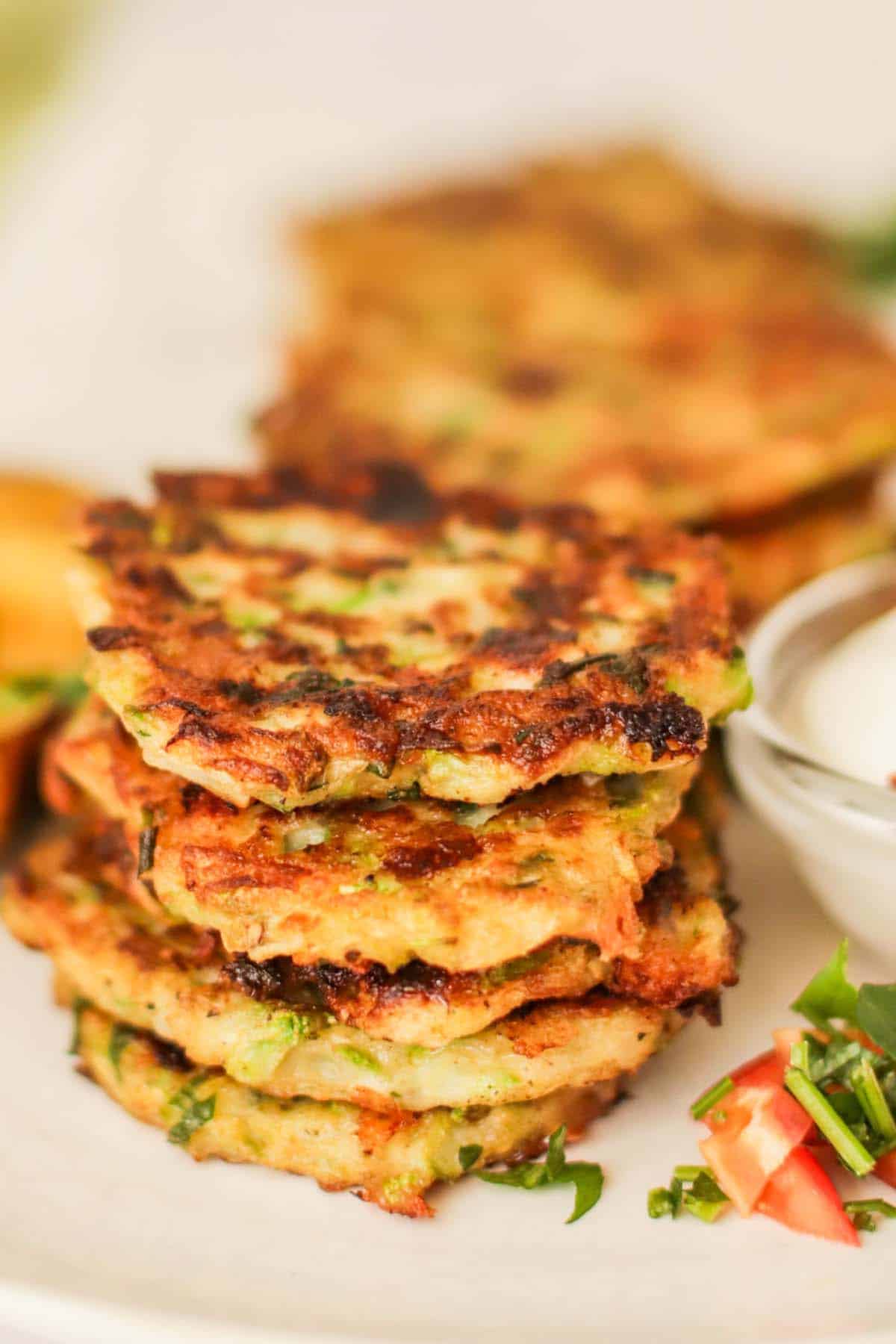 Zucchini fritters stacked on a plate next to a dipping sauce.