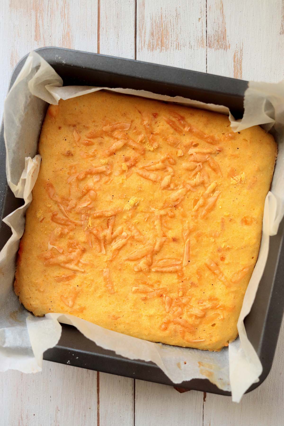 Baked cornbread in a baking pan lined with parchment paper.