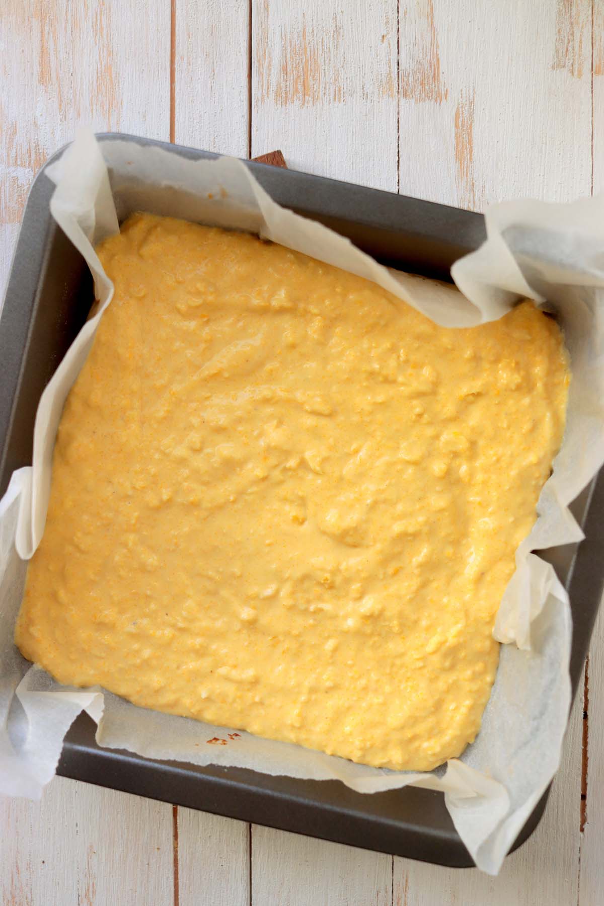 Cornbread batter in a baking pan lined with parchment paper.